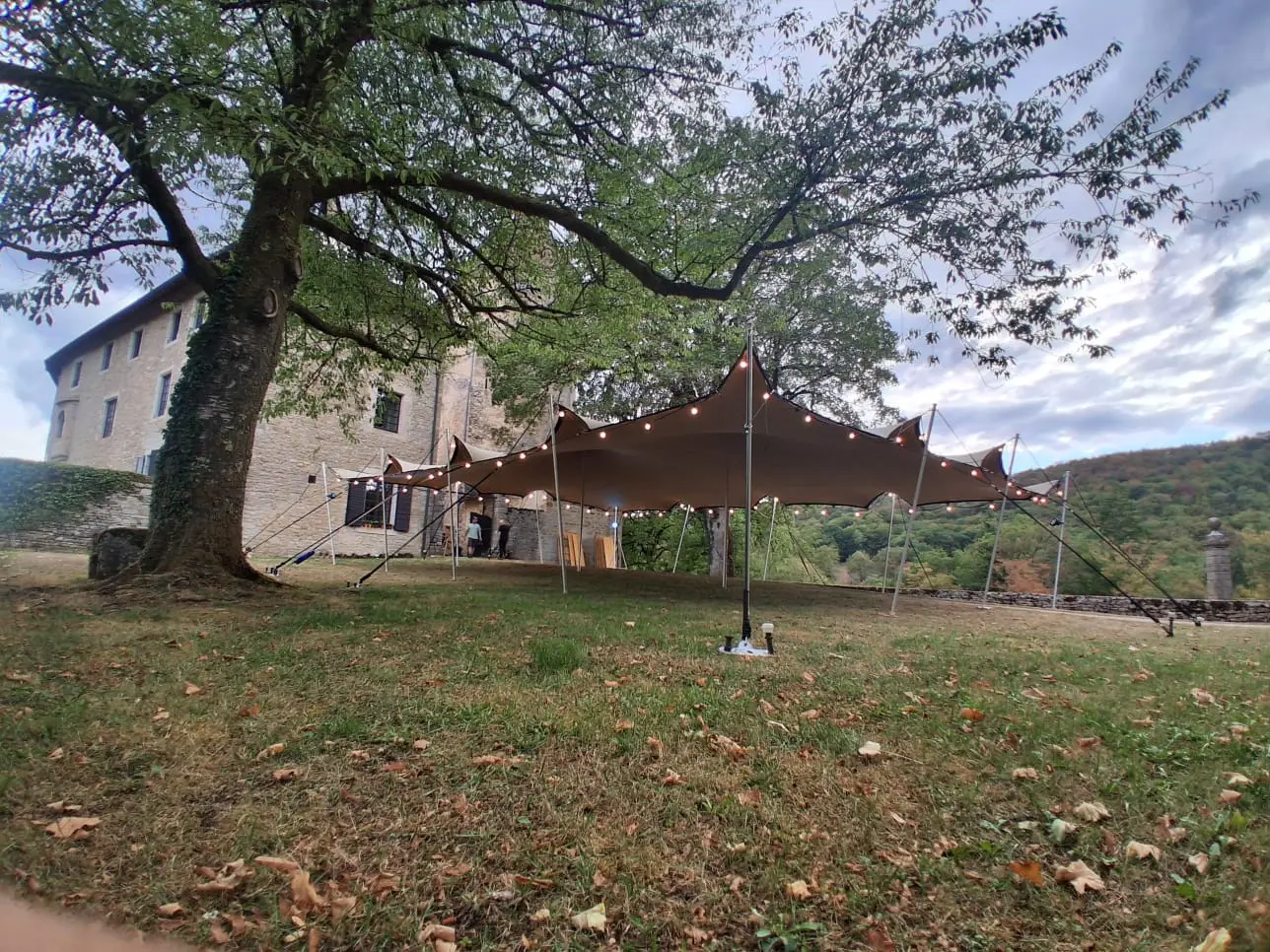 Toile d’ombrage brune tendue sous les arbres près d’un bâtiment en pierre