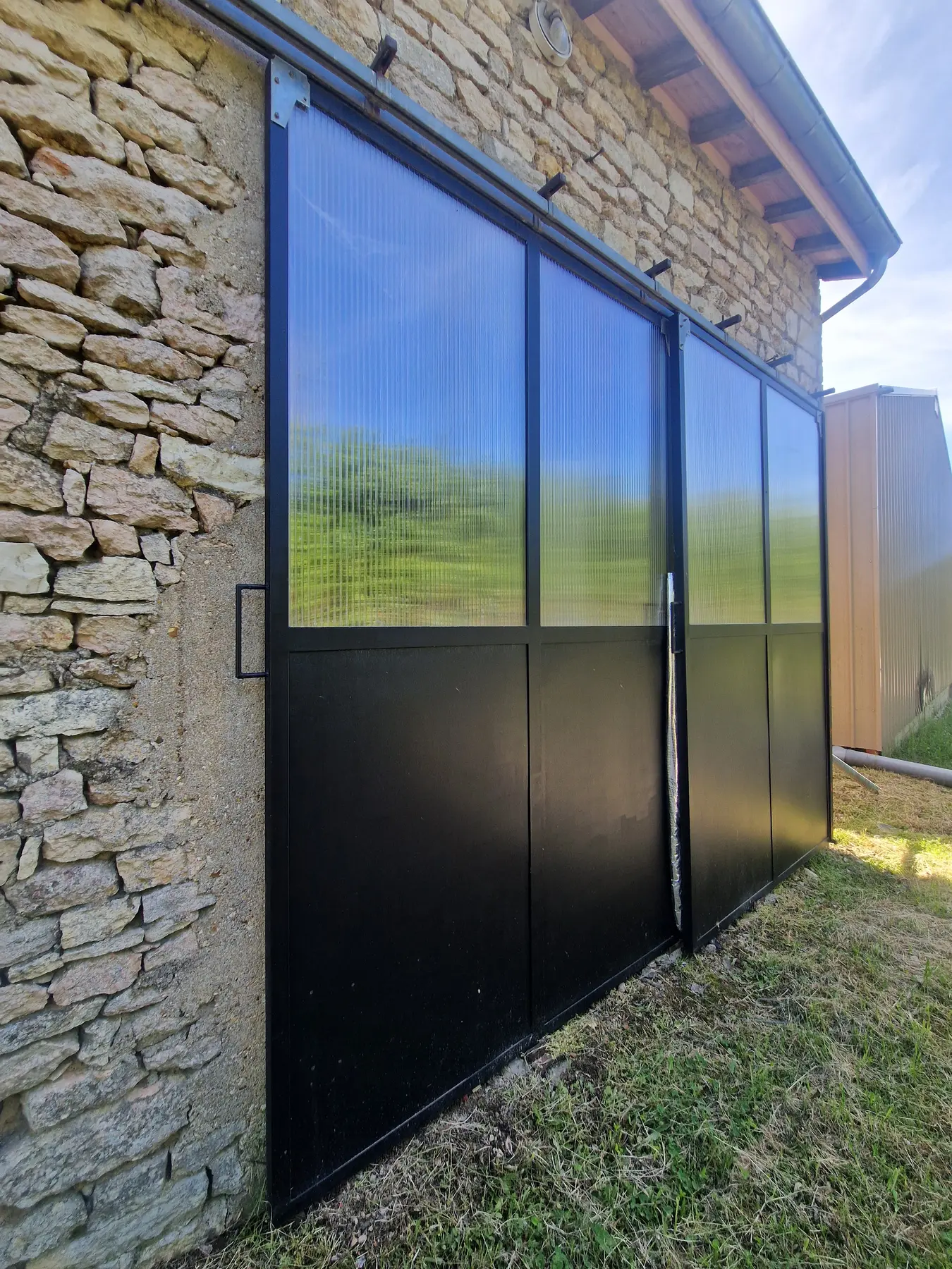 Grandes portes coulissantes en métal et panneaux translucides sur un bâtiment en pierre