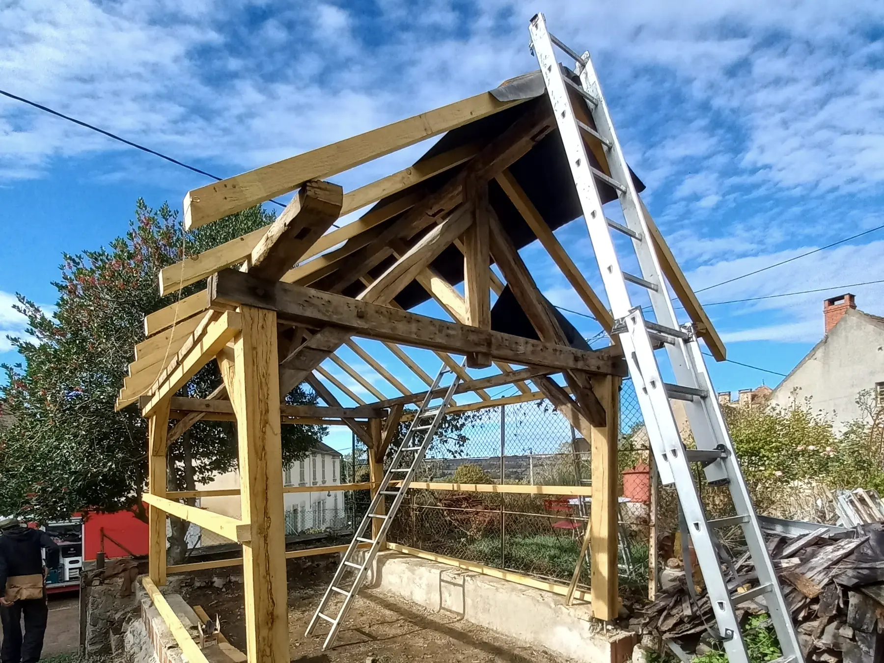 Charpente bois d’un abri en cours de montage avec échelles sur le chantier