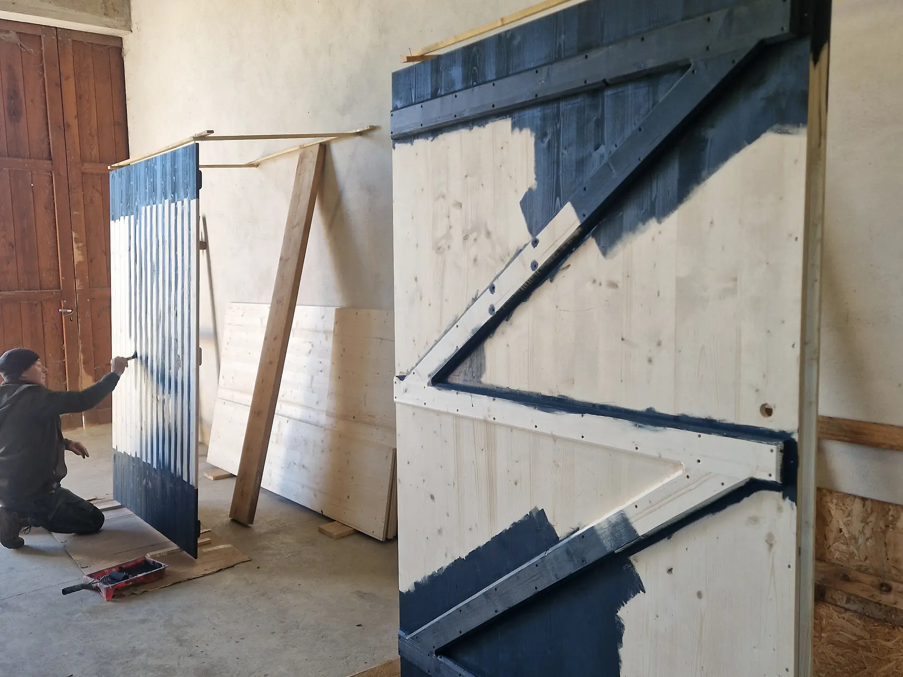 Grandes portes en bois avec ferrures sombres pendant leur mise en finition dans l’atelier